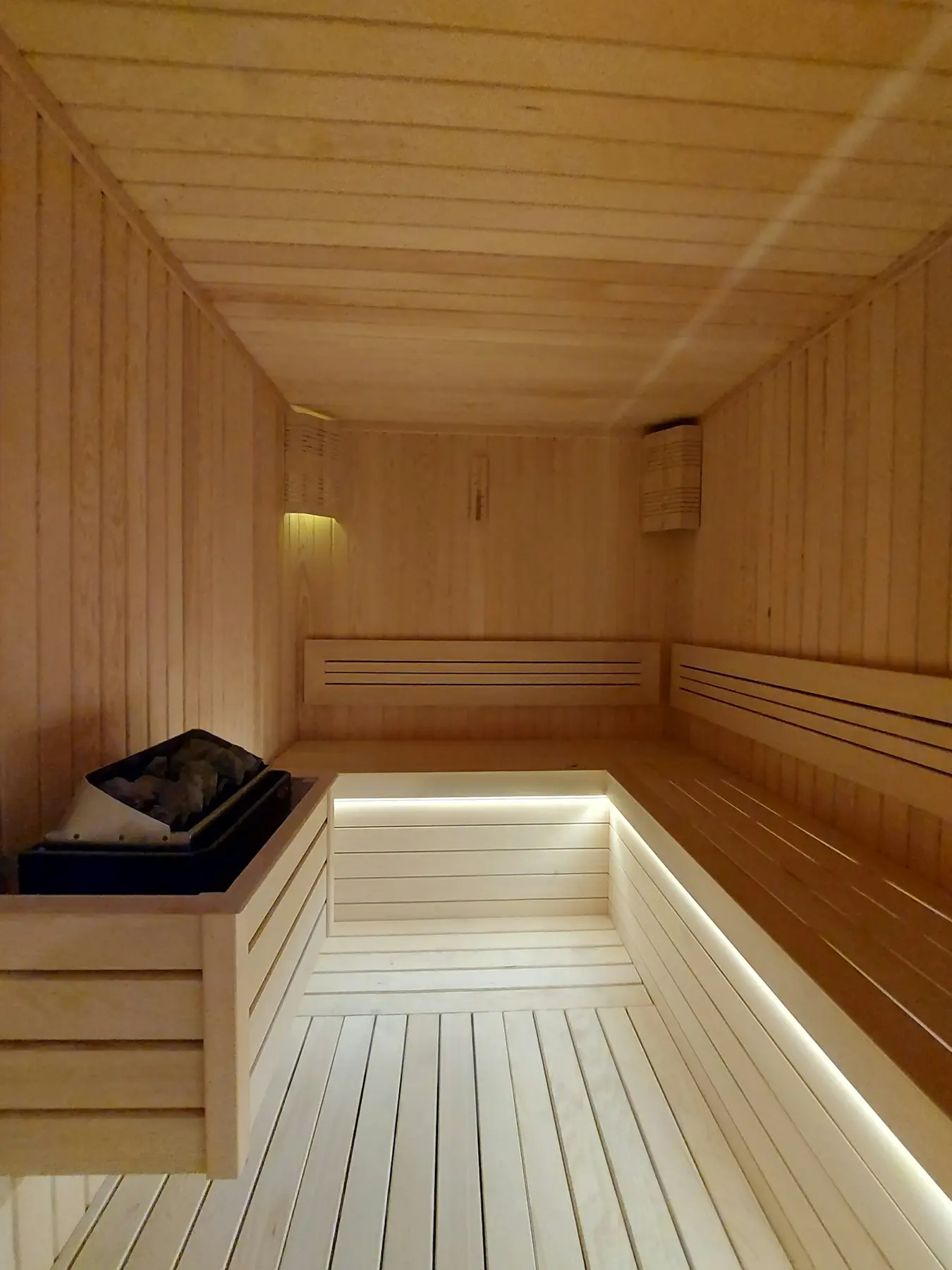 Úzká světlá sauna s podsvícenými dřevěnými lavicemi